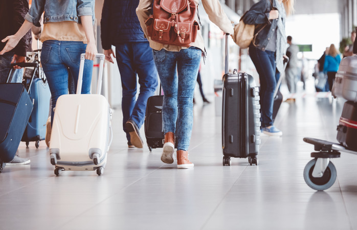 Reizigers op een vliegveld met verschillende formaten koffers en trolleys.