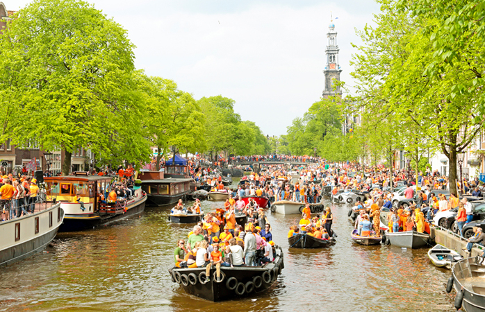 Mensen vieren Koningsdag op de grachten van Amsterdam.
